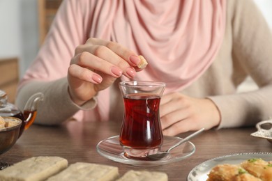 Photo of Woman with cup of delicious Turkish tea at wooden table, closeup