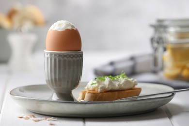 Photo of Fresh soft boiled egg in cup and sandwich on white wooden table