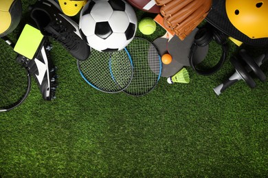 Different sports equipment on green grass, flat lay. Space for text