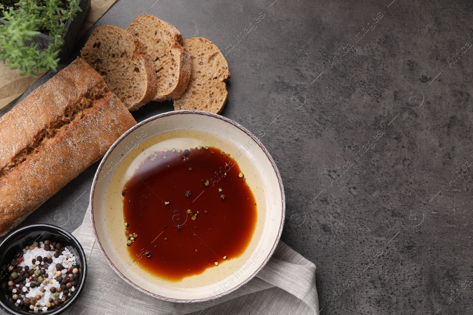 Photo of Bowl of balsamic vinegar with oil, spices and bread on dark grey table, flat lay. Space for text