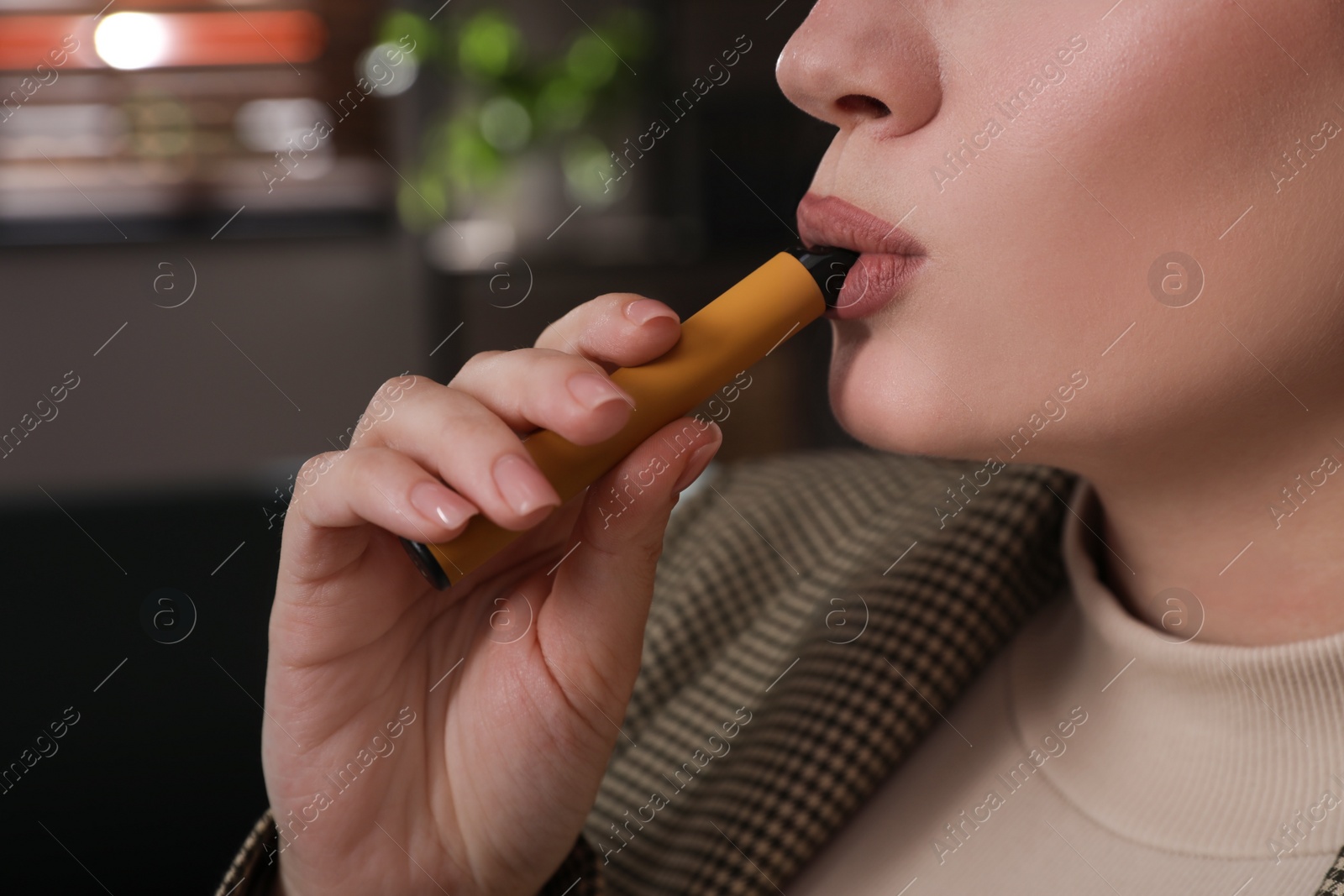 Photo of Young woman using disposable electronic cigarette indoors, closeup