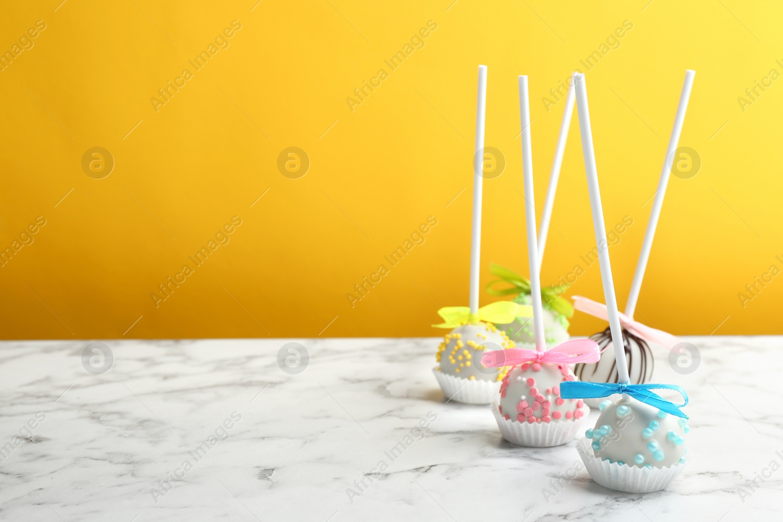 Photo of Different tasty cake pops on white marble table against yellow background. Space for text