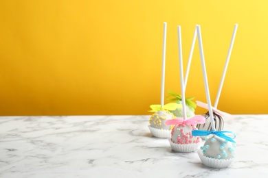 Different tasty cake pops on white marble table against yellow background. Space for text