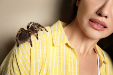 Photo of Scared young woman with tarantula on beige background, closeup. Arachnophobia (fearspiders)