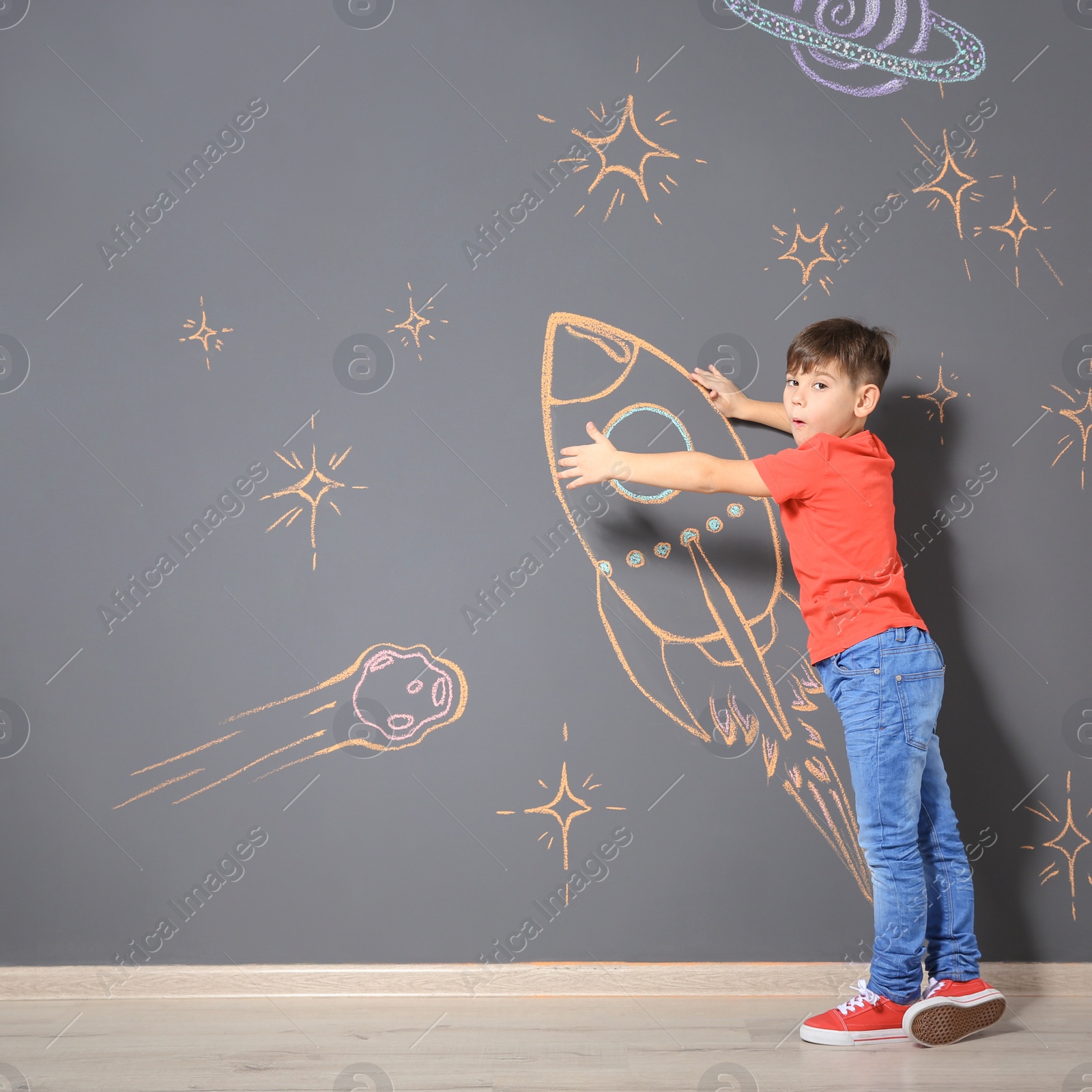 Photo of Cute little child playing with chalk rocket drawing on grey wall