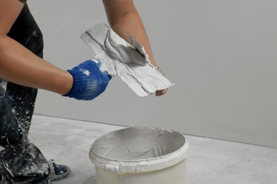 Photo of Professional worker putting plaster on putty knife indoors, closeup