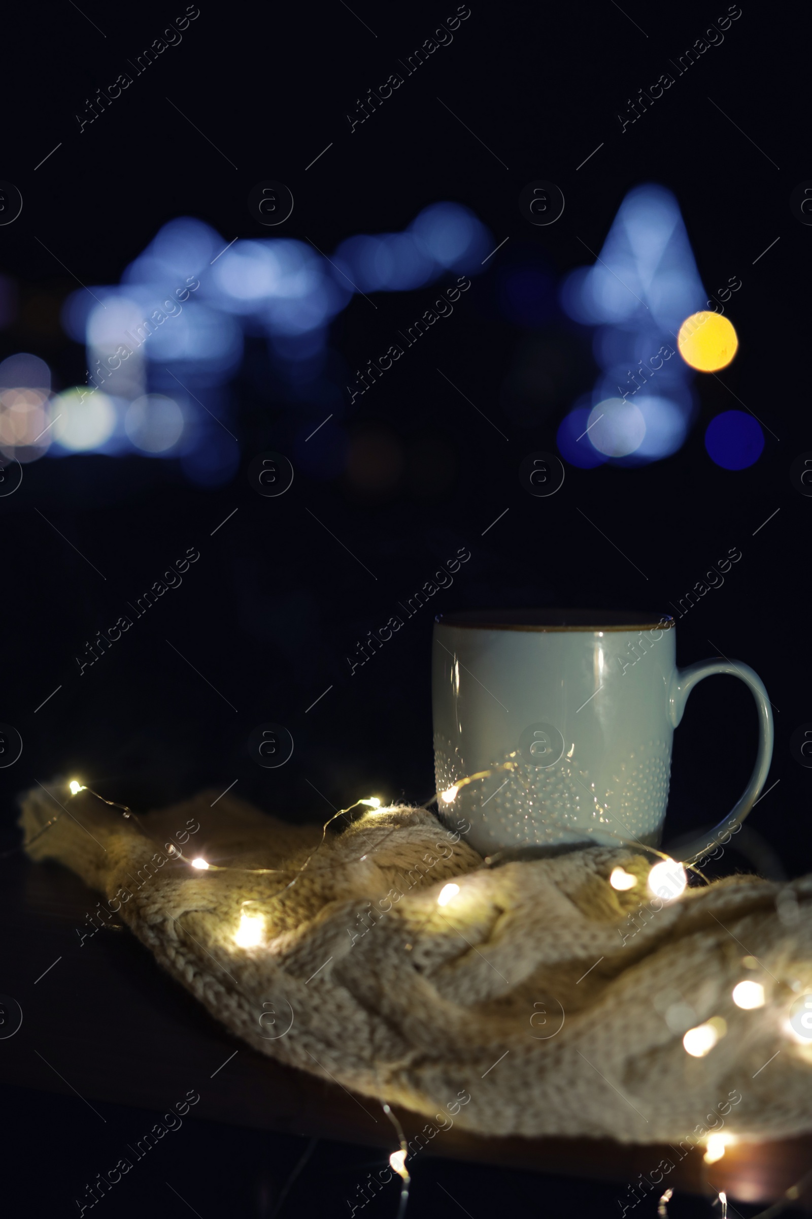 Photo of Cup of hot beverage, sweater and Christmas lights outdoors on winter night