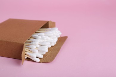 Photo of Box with wooden cotton buds on pink background. Space for text