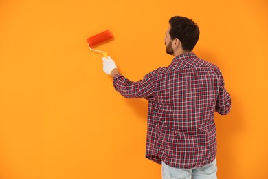 Photo of Designer painting orange wall with roller, back view. Space for text
