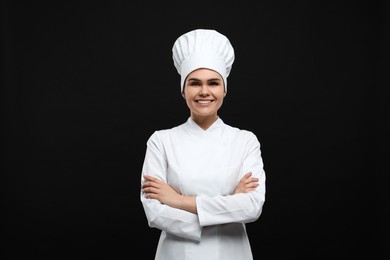 Happy female chef wearing uniform and cap on black background