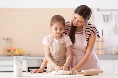 Mother and her daughter preparing dough at table in kitchen