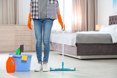 Young woman with mop and detergents in bedroom, closeup. Cleaning service