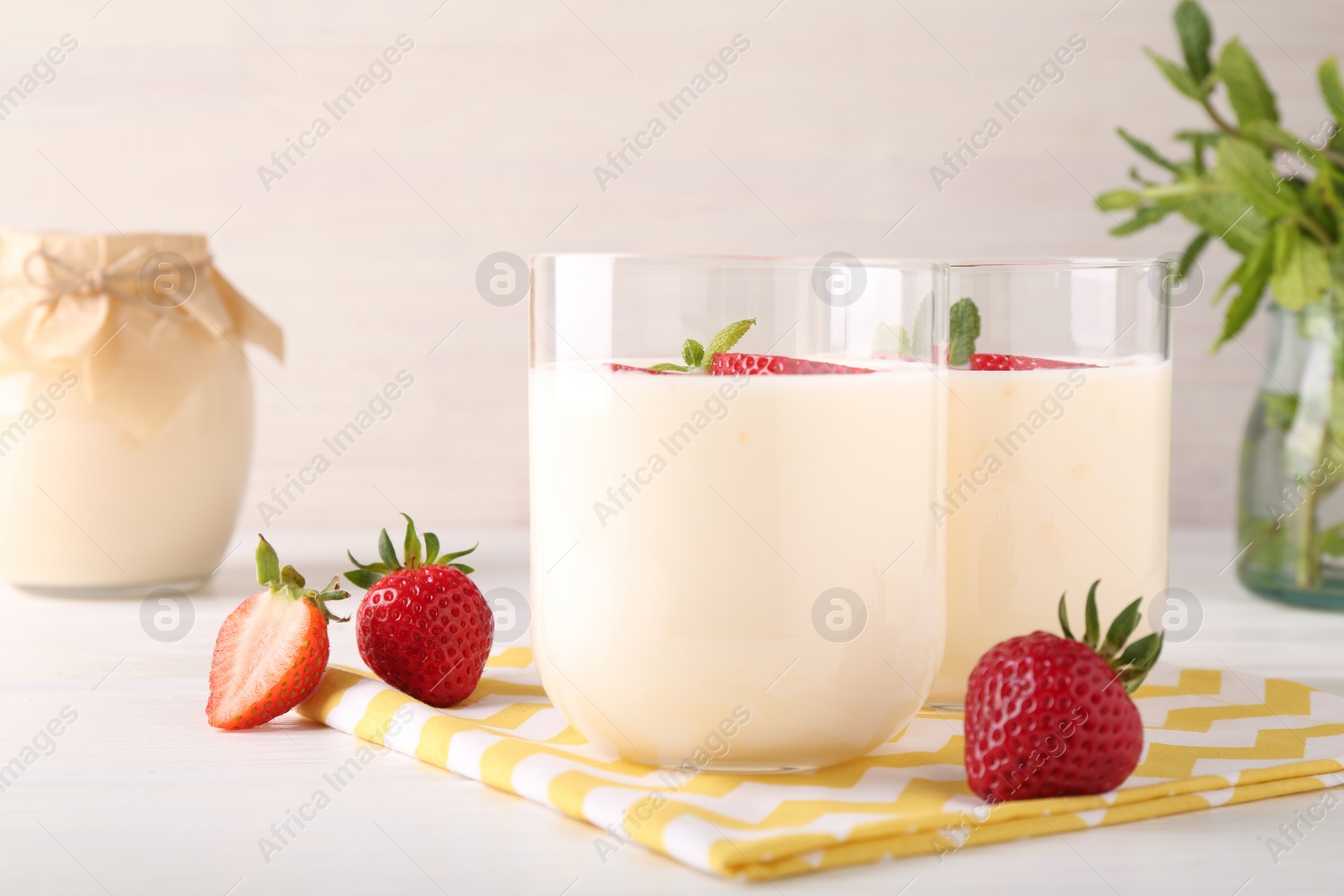 Photo of Tasty yogurt and strawberries in glasses on white wooden table, closeup