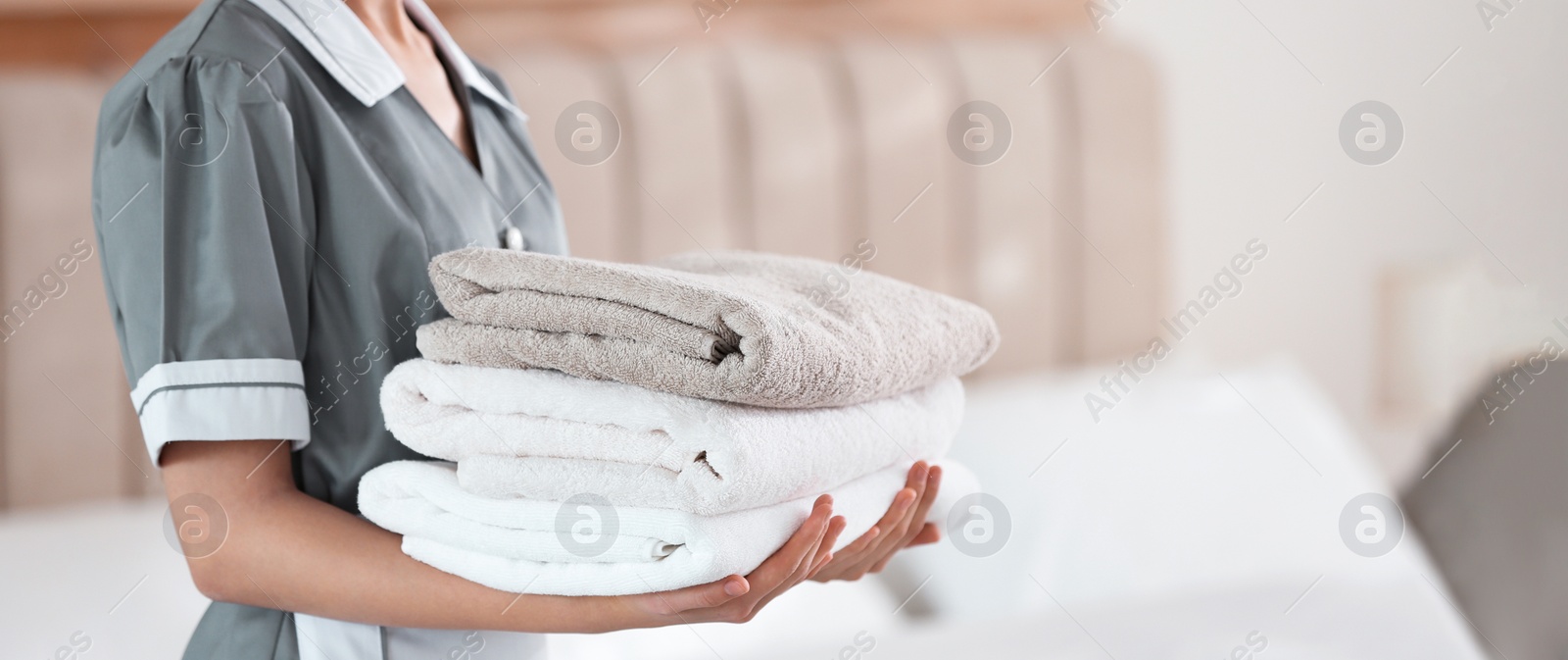 Image of Young chambermaid holding stack of fresh towels in bedroom, closeup. Banner design