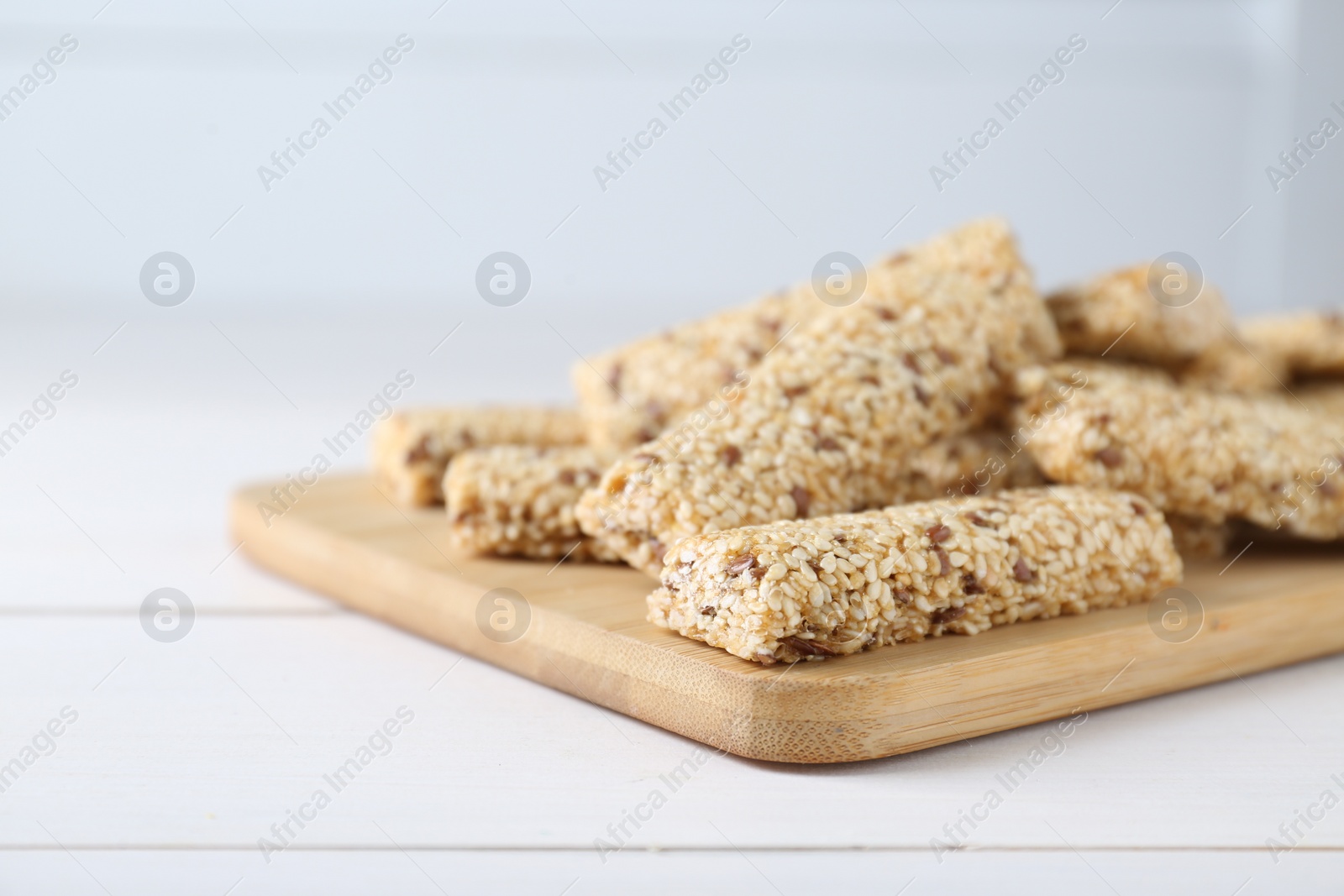 Photo of Tasty sesame seed bars on white wooden table, closeup. Space for text