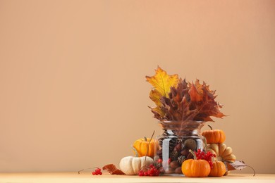 Photo of Composition with beautiful autumn leaves, berries and pumpkins on table against beige background, space for text