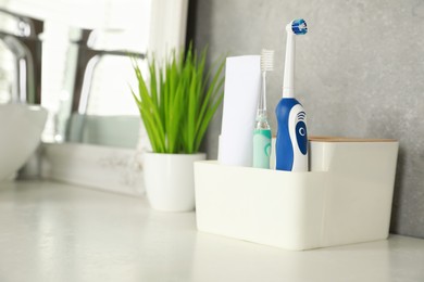 Photo of Electric toothbrushes and tube of paste on white countertop in bathroom. Space for text