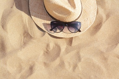 Photo of Hat with beautiful sunglasses on sand, top view. Space for text