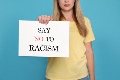 Photo of Young woman holding sign with phrase Say No To Racism on light blue background, closeup