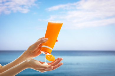 Young woman applying sun protection cream near sea, closeup