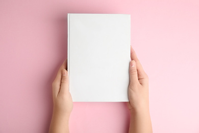 Photo of Woman holding book with blank cover on pink background, top view