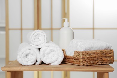 Photo of Soft folded terry towels and cosmetic bottle on wooden table indoors