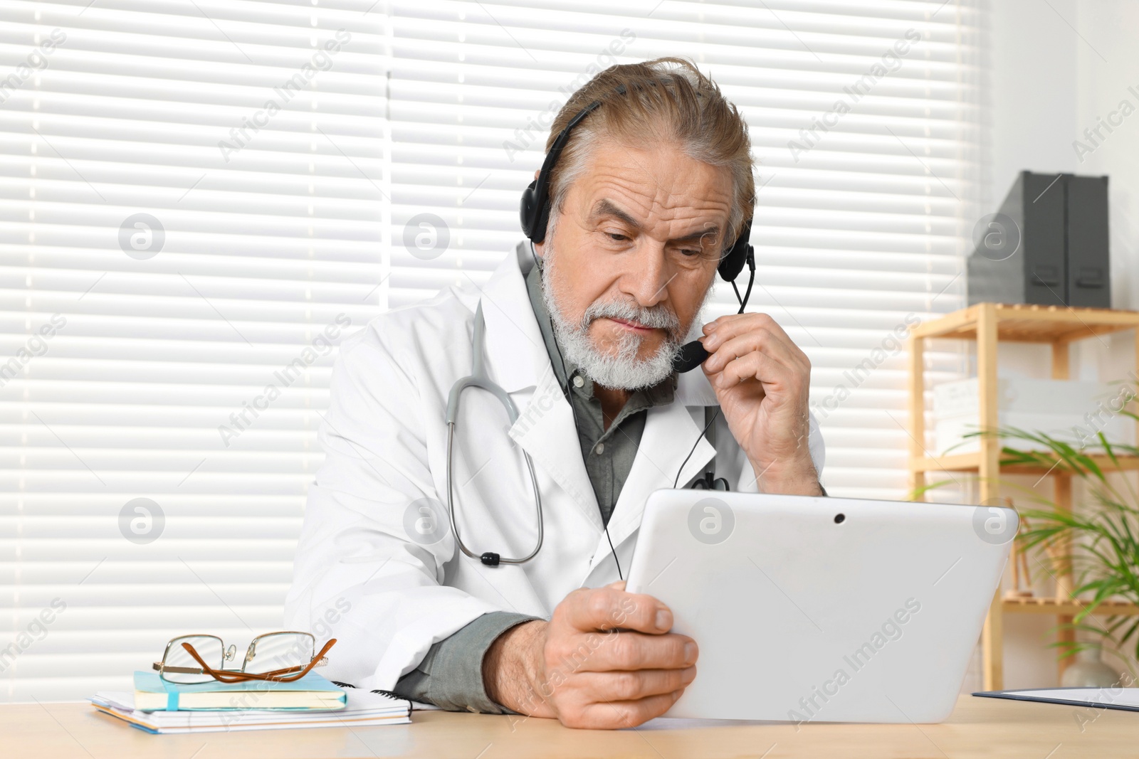 Photo of Senior doctor with tablet consulting patient at wooden desk in clinic. Online medicine