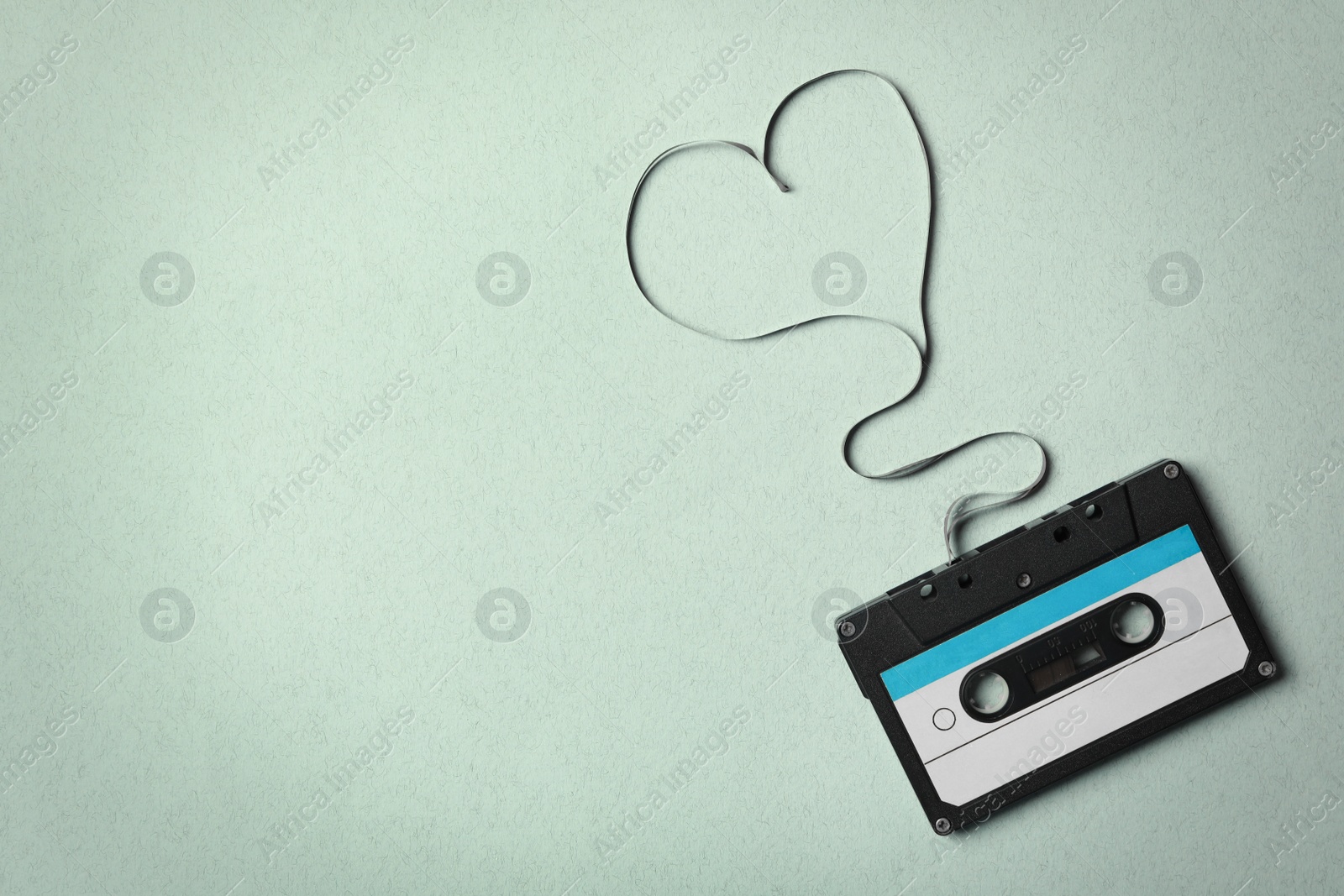 Photo of Top view of music cassette and heart made with tape on turquoise background, space for text. Listening love song