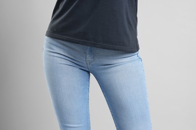 Woman wearing stylish jeans on light gray background, closeup