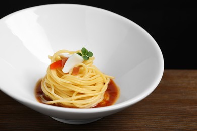 Photo of Tasty spaghetti with sauce on wooden table, closeup. Exquisite presentation of pasta dish