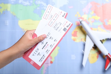Woman holding airline tickets above world's map with toy plane, closeup. Travel agency concept