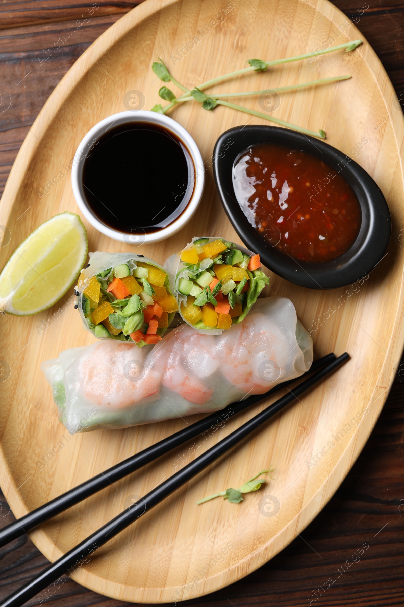 Photo of Tasty spring rolls and sauces on wooden table, top view