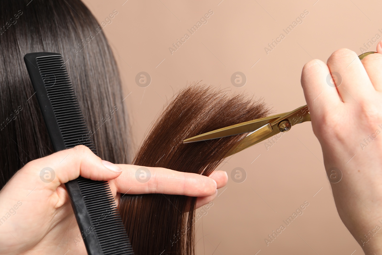 Photo of Hairdresser cutting client's hair with scissors on beige background, closeup