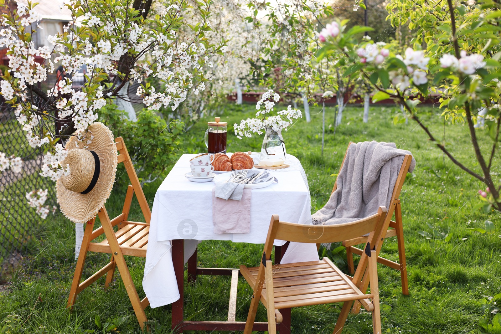 Photo of Stylish table setting with beautiful spring flowers, tea and croissants in garden