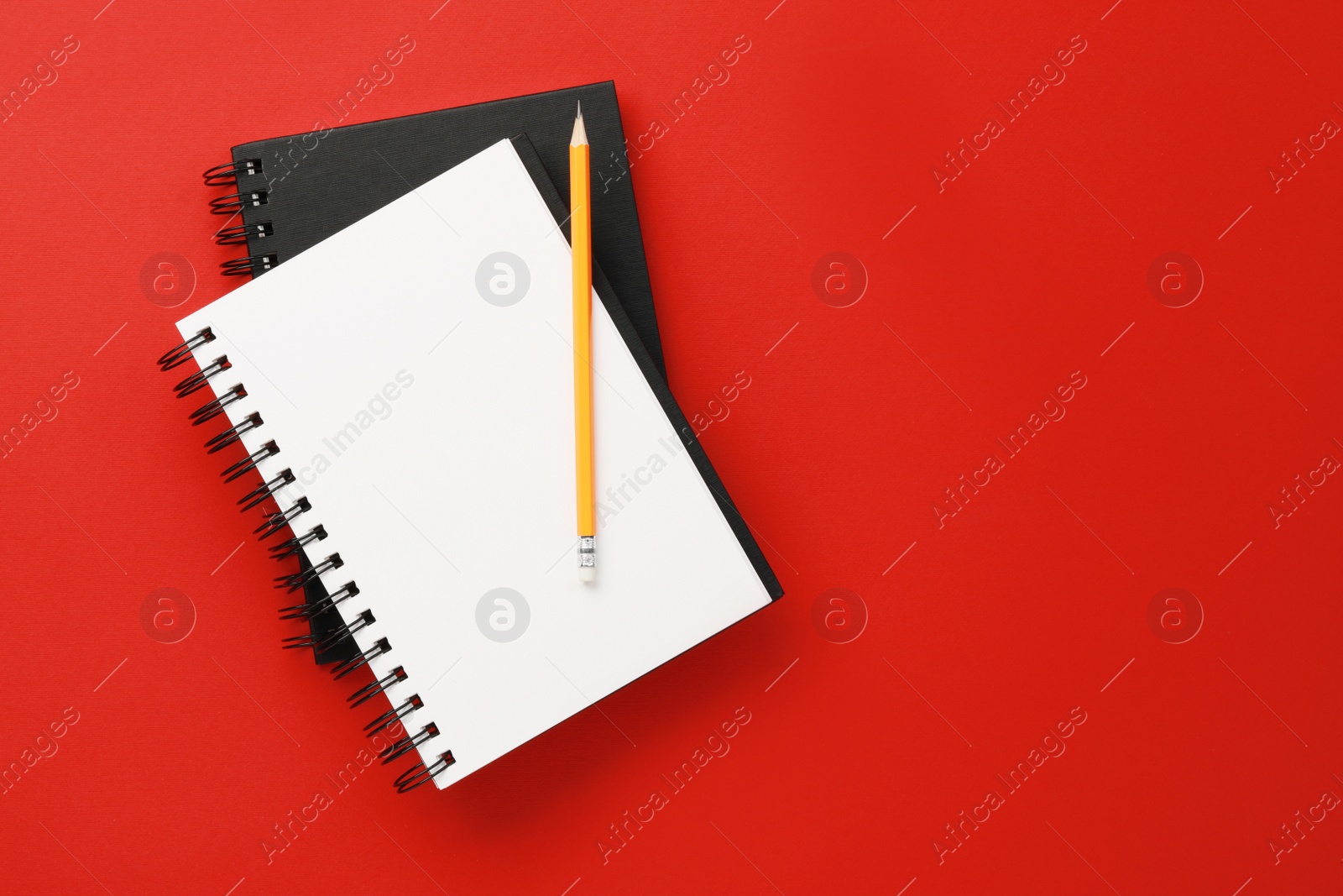 Photo of Notebooks and pencil on red background, top view. Space for text