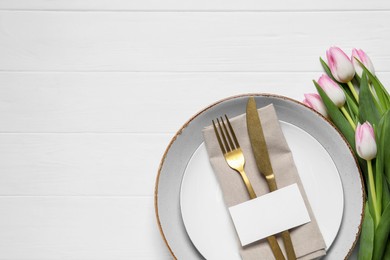 Photo of Stylish table setting with cutlery, paper card and tulips on white wooden background, flat lay. Space for text