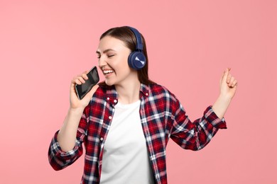 Photo of Happy woman in headphones enjoying music and dancing with smartphone on pink background