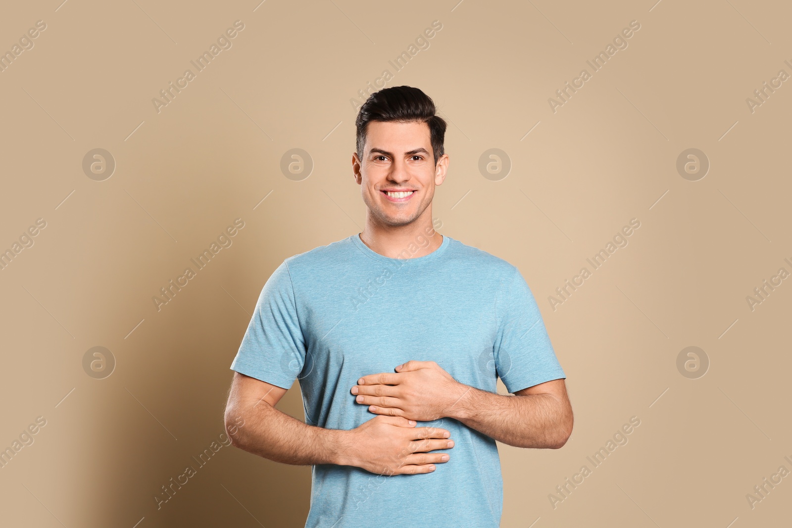 Photo of Happy healthy man touching his belly on beige background