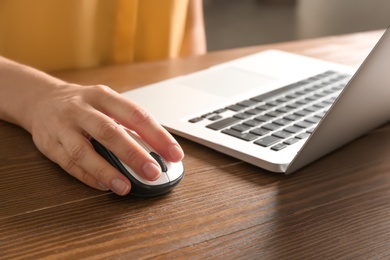 Woman using computer mouse with laptop at table, closeup