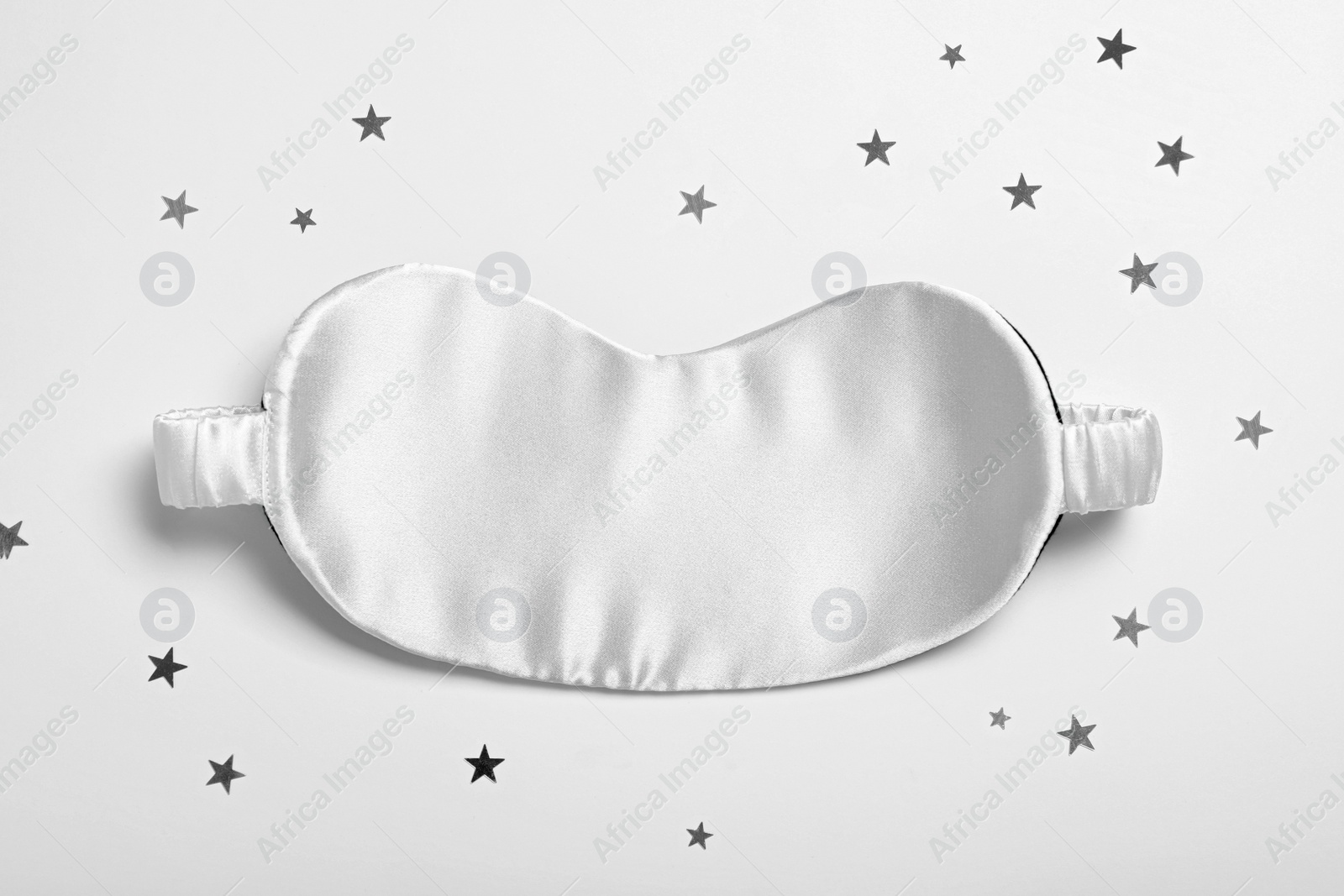 Photo of Sleeping mask and glitter on white background, top view. Bedtime accessory