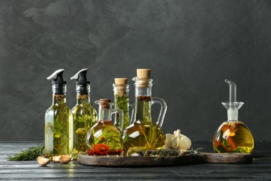 Photo of Cooking oil with different spices and herbs in bottles on grey wooden table