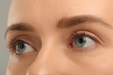 Woman with beautiful natural eyelashes on grey background, closeup