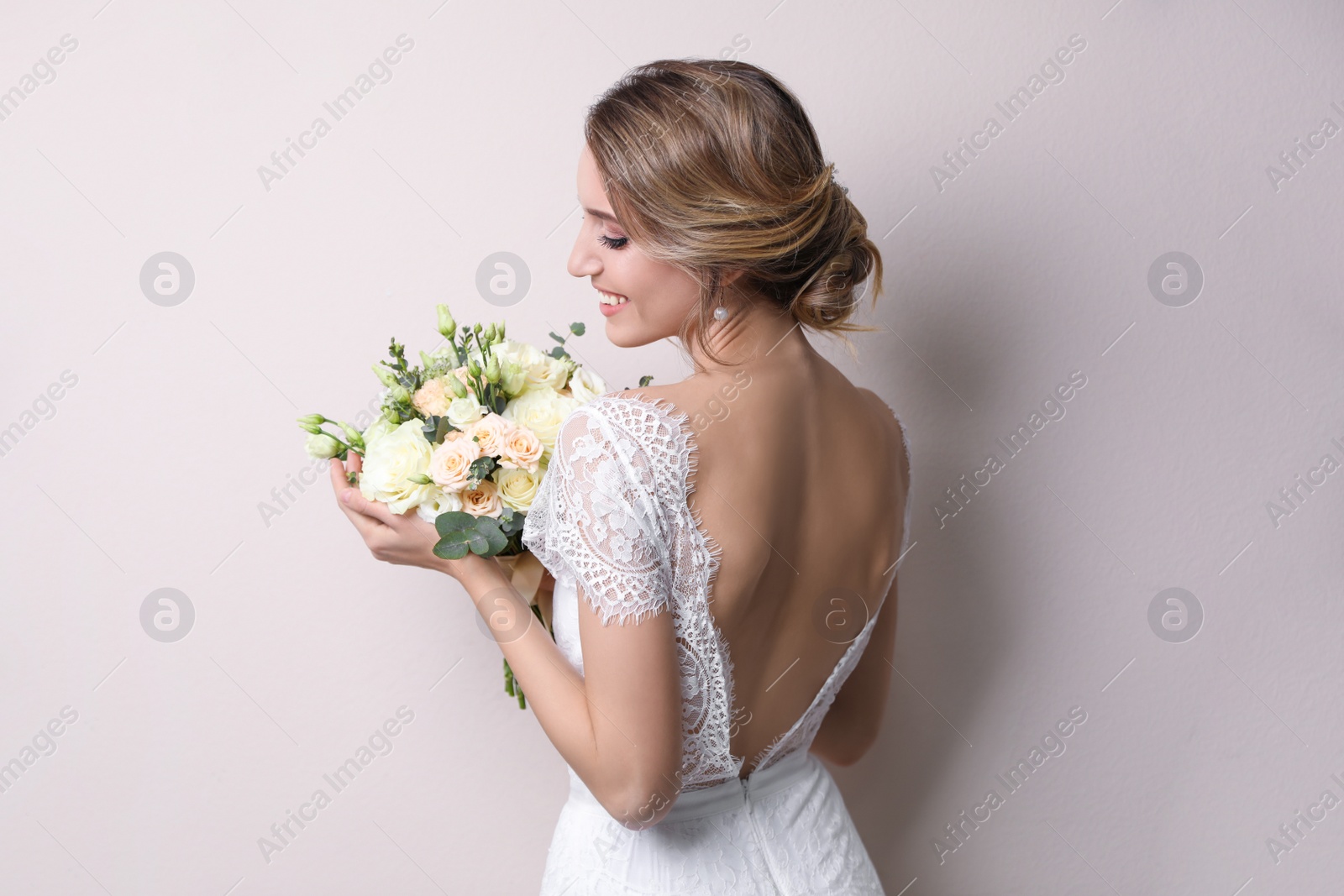 Photo of Young bride with elegant hairstyle holding wedding bouquet on beige background