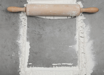 Flour and rolling pin on light grey table, top view. Space for text