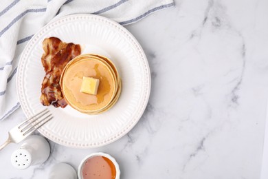 Delicious pancakes with butter, maple syrup and fried bacon served on white marble table, flat lay. Space for text