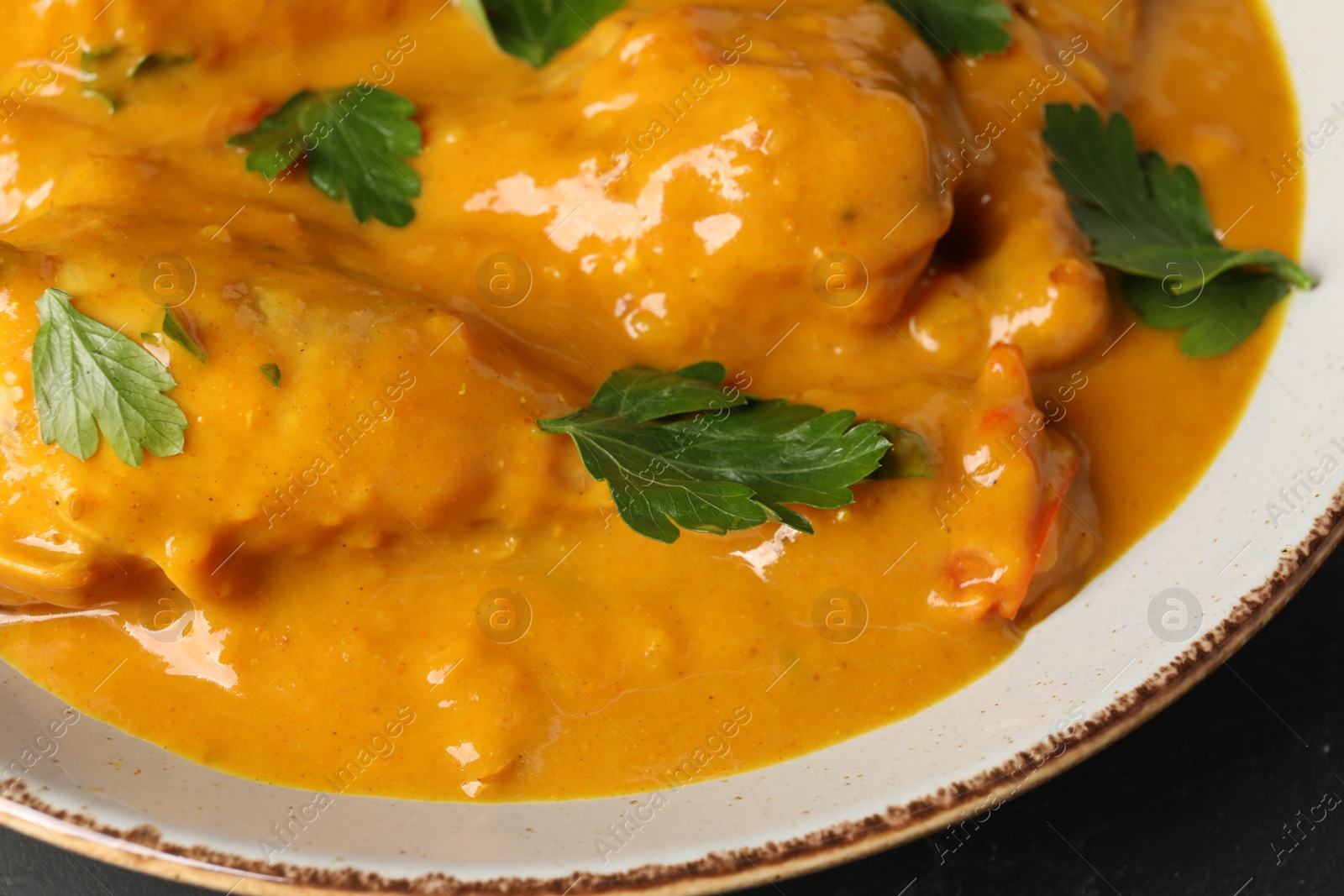 Photo of Tasty chicken curry with parsley on black table, closeup