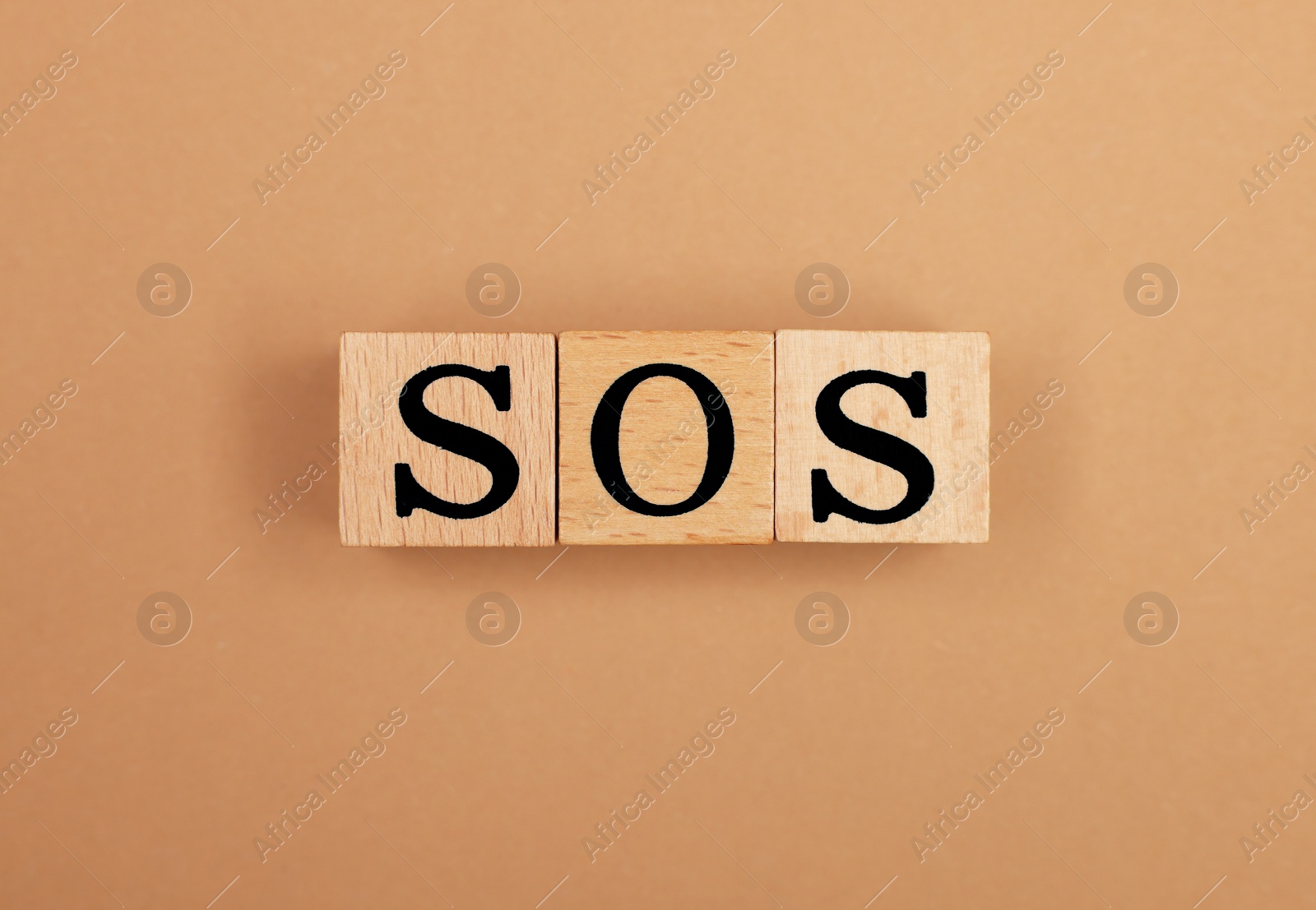 Photo of Abbreviation SOS made of wooden cubes on light brown background, top view