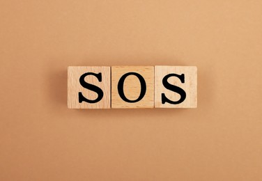 Photo of Abbreviation SOS made of wooden cubes on light brown background, top view