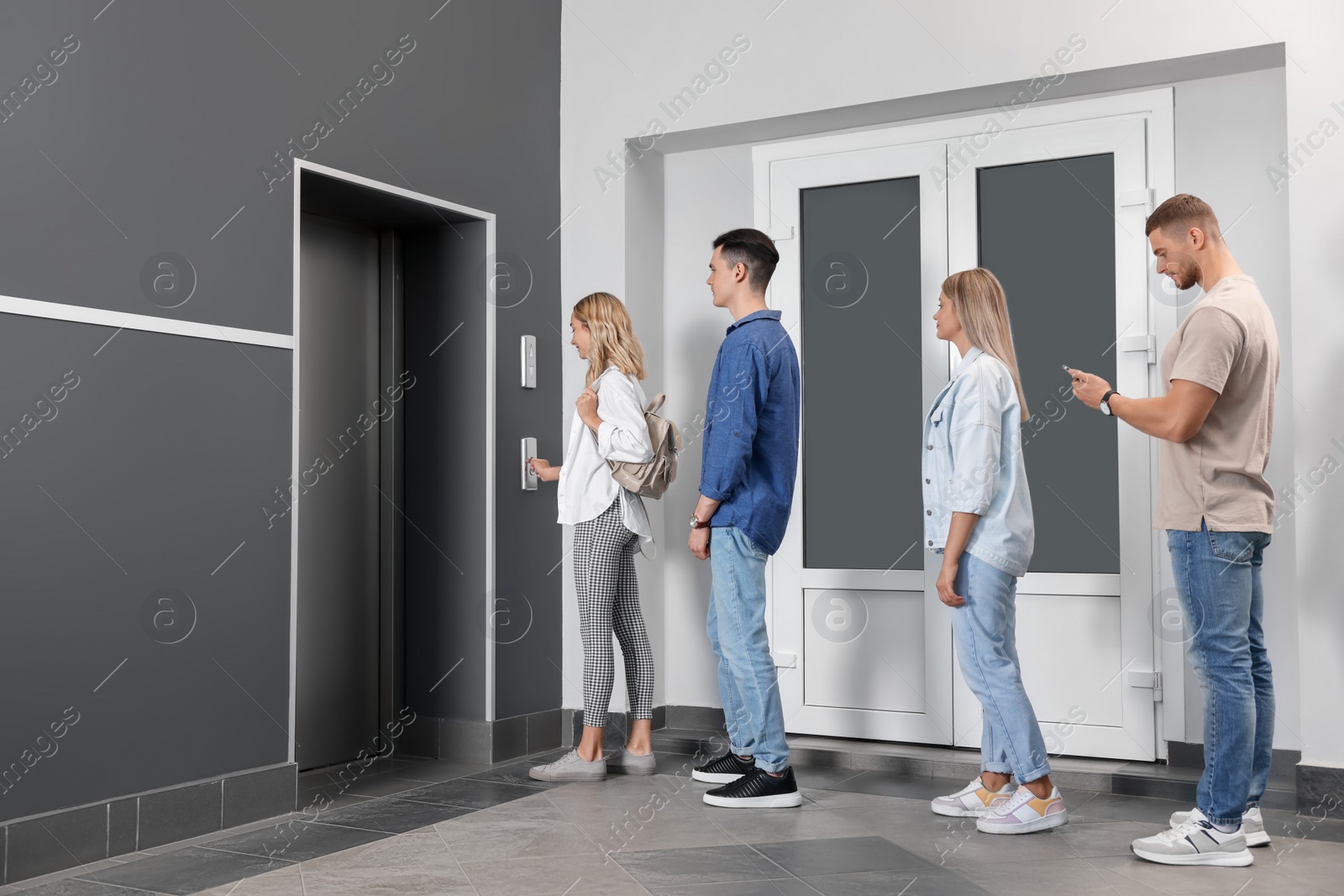 Photo of Group of people waiting in line for elevator while woman pressing call button