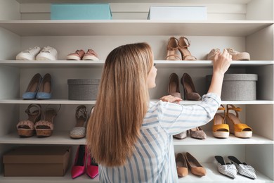 Photo of Woman near rack with shoes indoors, back view. Interior design